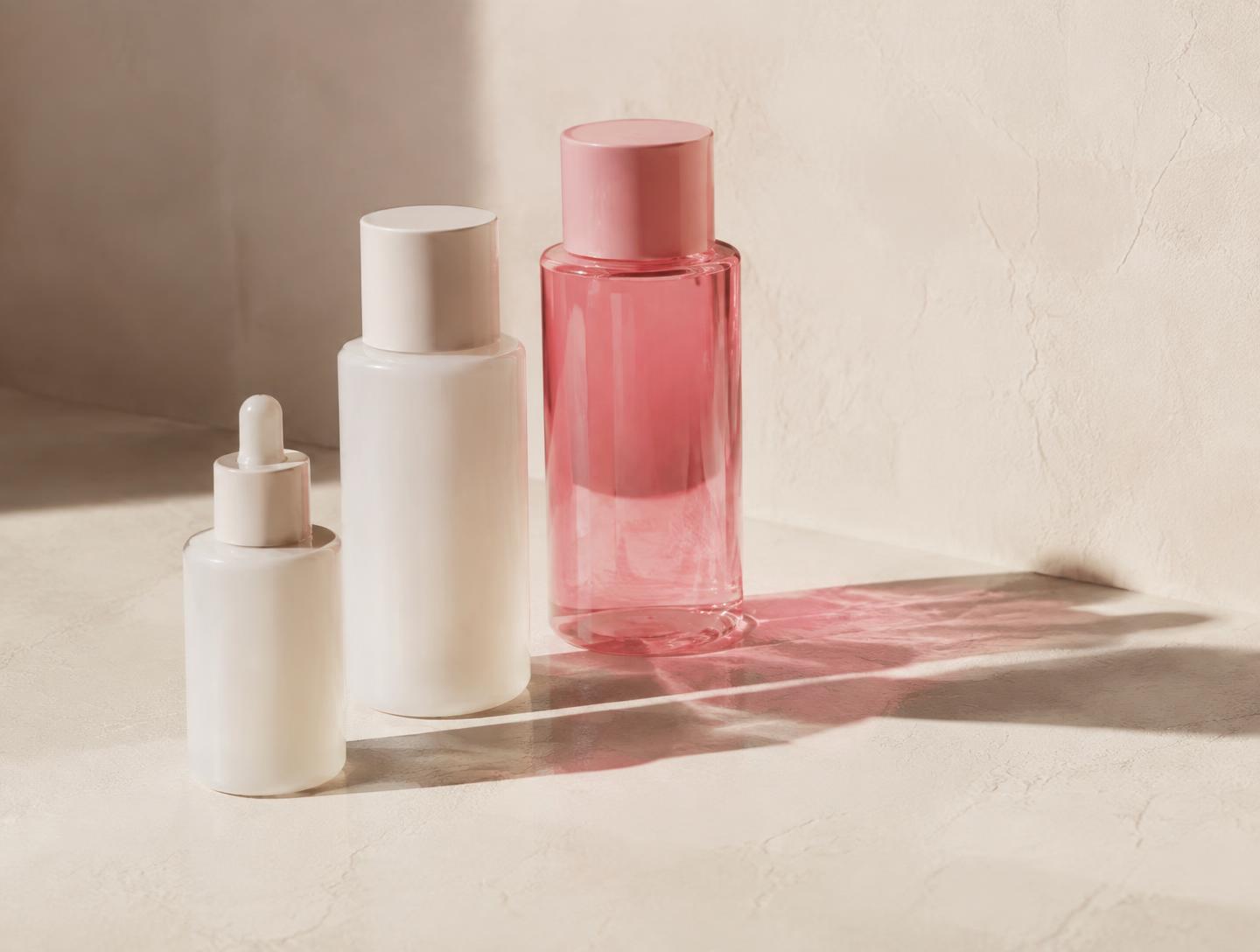 Minimal LUMÉ skincare bottles on a warm plaster surface with a pink cast shadow